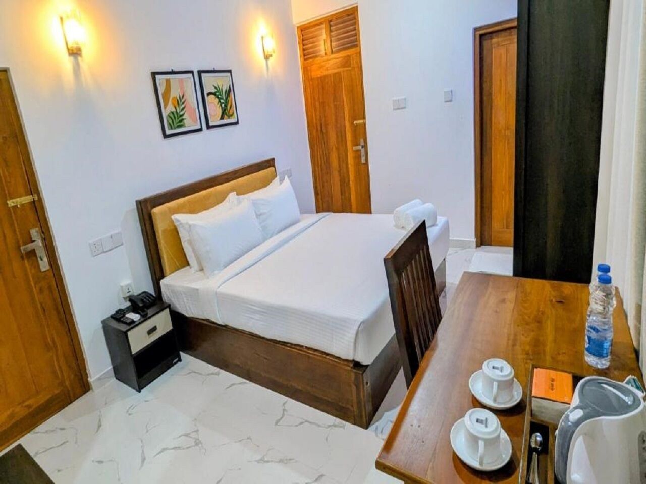 Une chambre d’hôtel avec un lit, une table de chevet et une petite table sur laquelle se trouvent des tasses et une bouilloire.