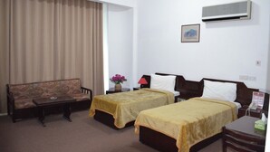 Een hotelkamer met twee eenpersoonsbedden, een bank, een tafeltje, een lamp, een airconditioner en een ingelijst schilderij aan de muur.