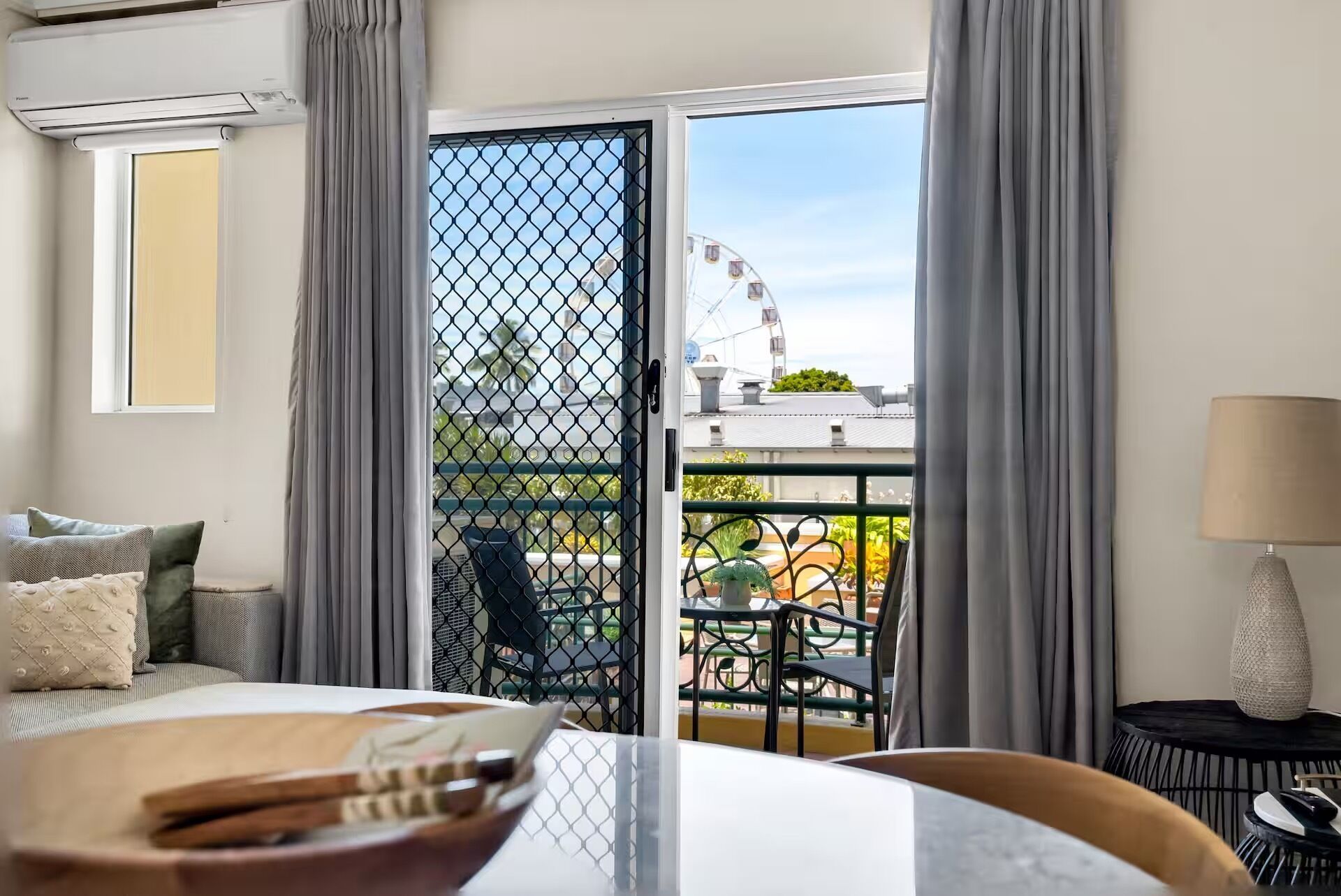 Ein Hotelzimmer mit Balkon, einem Esstisch, einem Stuhl, einer Lampe und Blick auf ein Riesenrad.