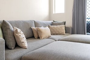 A sectional sofa with multiple cushions, a window with curtains, and a view of the outdoors. - Juliette’s View | Boutique Stay Near Esplanade (Cairns City)