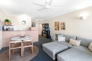 A modern living space with a dining area, a sofa, a ceiling fan, and a kitchen in the background. - Juliette’s View | Boutique Stay Near Esplanade (Cairns City)