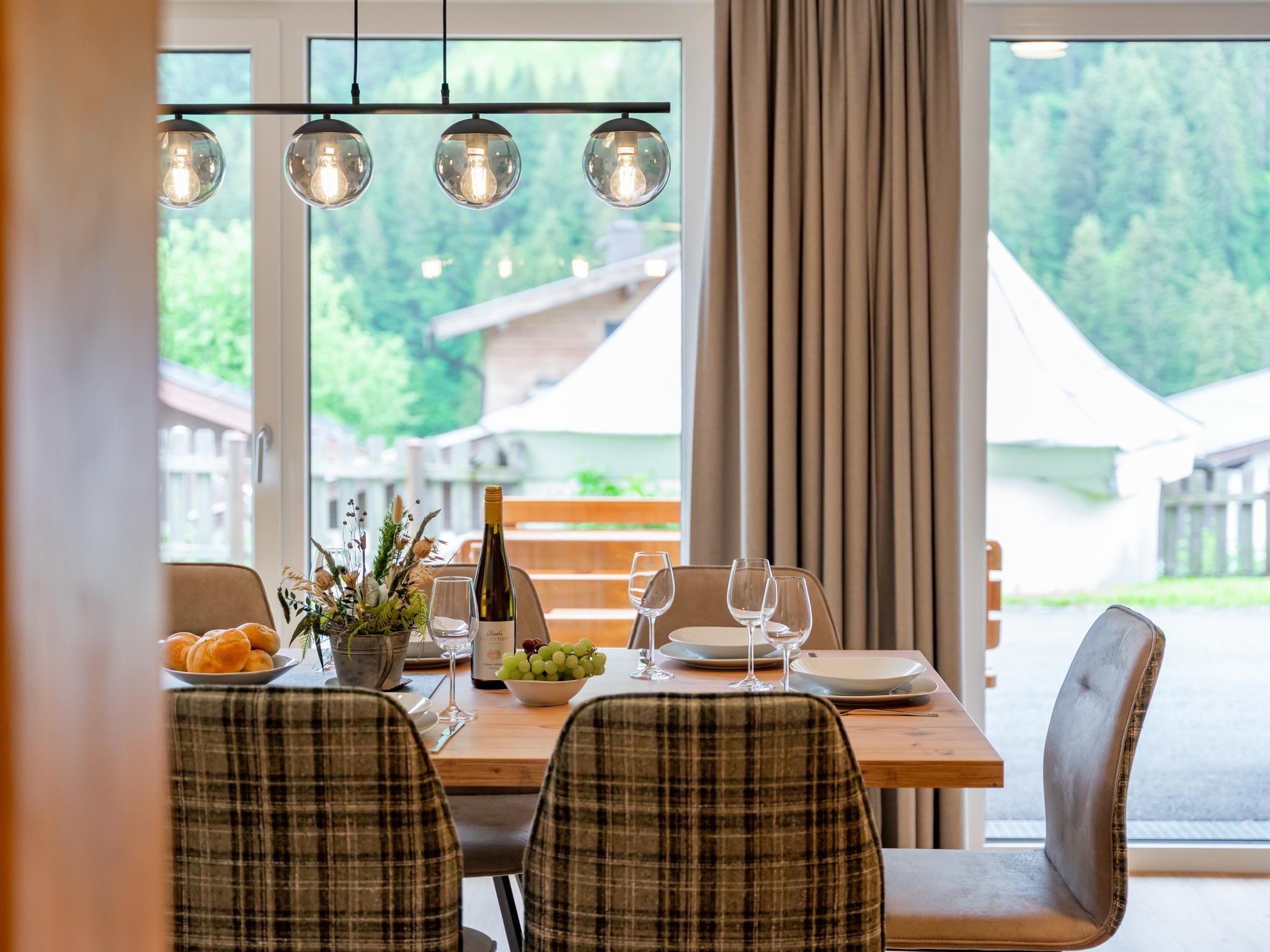 A dining area with a table set for four, featuring plaid chairs, a bottle of wine, and a bowl of grapes.