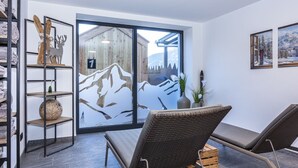 Ein Zimmer mit Blick auf Berge durch eine Glastür, ein Korbstuhl, ein Regal mit Handtüchern und eine Vase mit Pflanzen.