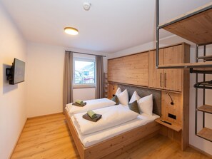 Ein modernes Schlafzimmer mit einem hölzernen Bett, einem an der Wand montierten Fernseher und einem Fenster mit Blick auf ein Gebäude.