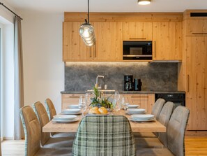 Eine moderne Küche mit Holzschränken, einer eingebauten Mikrowelle und einem Essbereich für sechs Personen, ausgestattet mit Tisch, Stühlen und einer Tischdekoration.