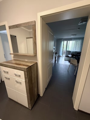 Ein Zimmer mit einem hölzernen Waschtisch, einem Spiegel und einer Tür zu einem Wohnbereich mit einer Couch und einem Tisch.