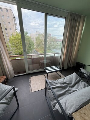 A modern apartment with a balcony, a sofa, a small table, and a view of a building and trees.
