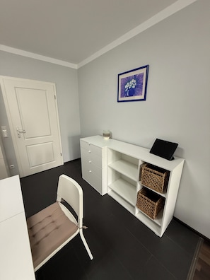 Une pièce avec un bureau blanc, une chaise, une porte et un tableau encadré au mur.
