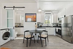 A modern kitchen with a dining table, chairs, a washing machine, and a refrigerator.