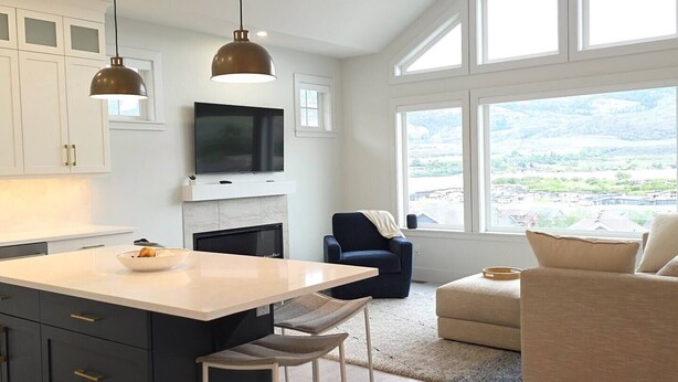 Eine moderne Küche mit einer großen Kochinsel, einem Flachbildfernseher und einem Kamin. Im Wohnbereich befindet sich eine Couch und ein Sessel mit Blick auf eine verschneite Landschaft.