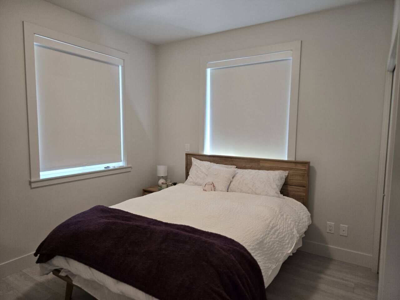 Un dormitorio con una cama, una mesita de noche, una lámpara y dos ventanas.