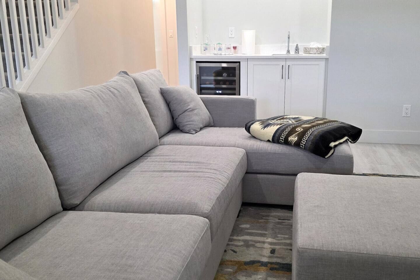 A modern living room with a grey sectional sofa, a small table, and a patterned throw blanket.