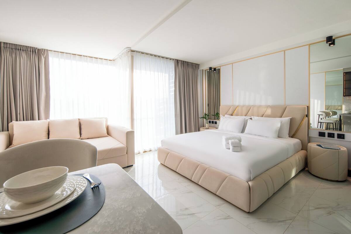 Una habitación de hotel moderna con una cama grande, un sofá, una mesa de comedor con un cuenco y un plato, y una mesita auxiliar.
