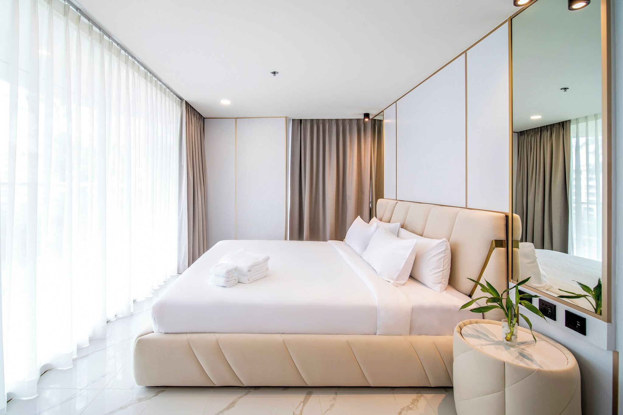 Ein modernes Hotelzimmer mit einem großen Bett, einem Nachttisch mit Pflanze und einem großen Spiegel.