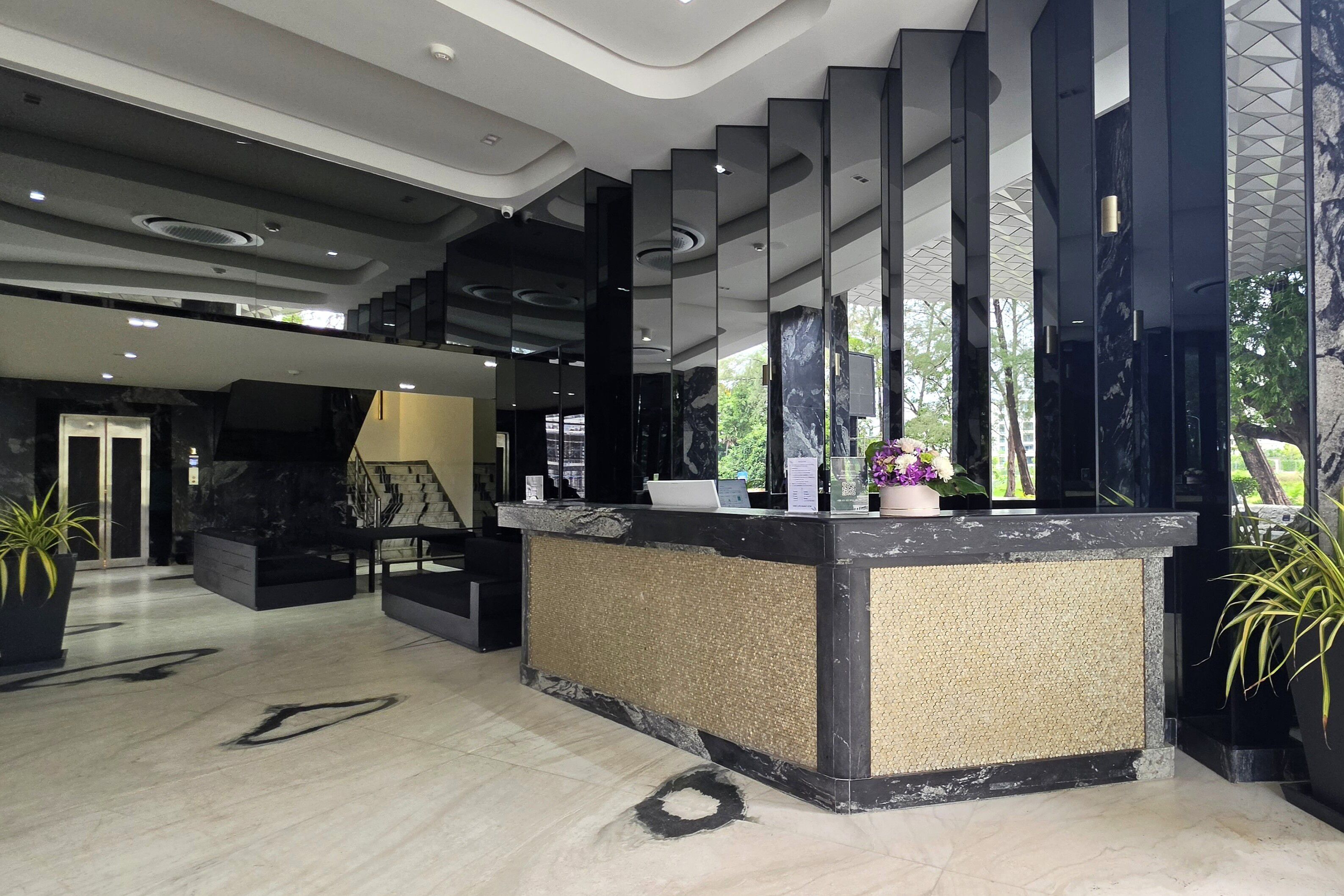 A modern reception area with a marble reception desk, a staircase, and a large window with a view of greenery.