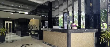 A modern reception area with a marble reception desk, a staircase, and a large window with a view of greenery.
