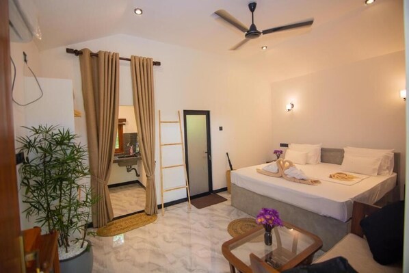 Une chambre d’hôtel avec un lit, un ventilateur de plafond, une petite table avec un vase et une plante en pot.