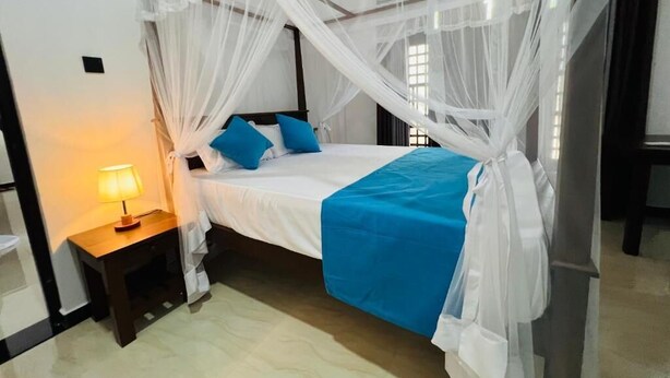 A bedroom with a canopy bed, a bedside table with a lamp, and a blue bedspread.
