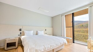 Ein modernes Hotelzimmer mit einem großen Bett, Nachttischen, einer Bank und einem großen Fenster mit Blick auf die Landschaft.