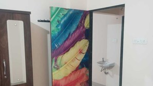 A room with a wooden wardrobe, a colorful abstract painting on the door, and a white sink.