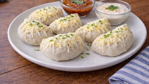 A plate of dumplings garnished with cheese and herbs, accompanied by two dipping sauces.