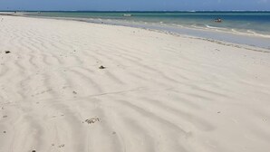 Ein weiter Sandstrand mit sanften Wellen, blauem Himmel und Booten in der Ferne.