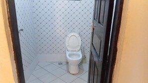 A small, tiled bathroom with a toilet, a shower area, and a door. - Tranquil 1-bedroom cottage with AC in Diani Beach (Diani Beach)