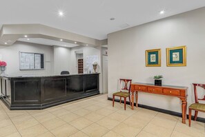 Ein Empfangsbereich mit Rezeption, einem Holztisch, zwei Stühlen und gerahmten Kunstwerken an der Wand.