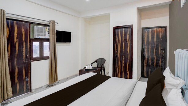 Ein Hotelzimmer mit einem Bett, einem Sessel, einem kleinen Tisch mit Tasse und Untertasse, einem an der Wand montierten Fernseher und einem Fenster mit Vorhängen.