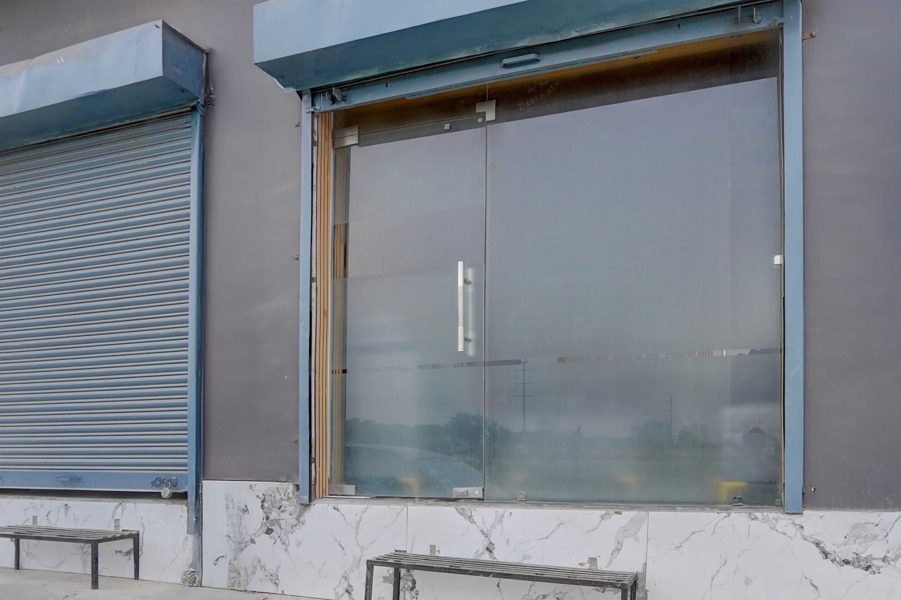 A building facade with a closed roller shutter door and a large glass window with a metal handle.