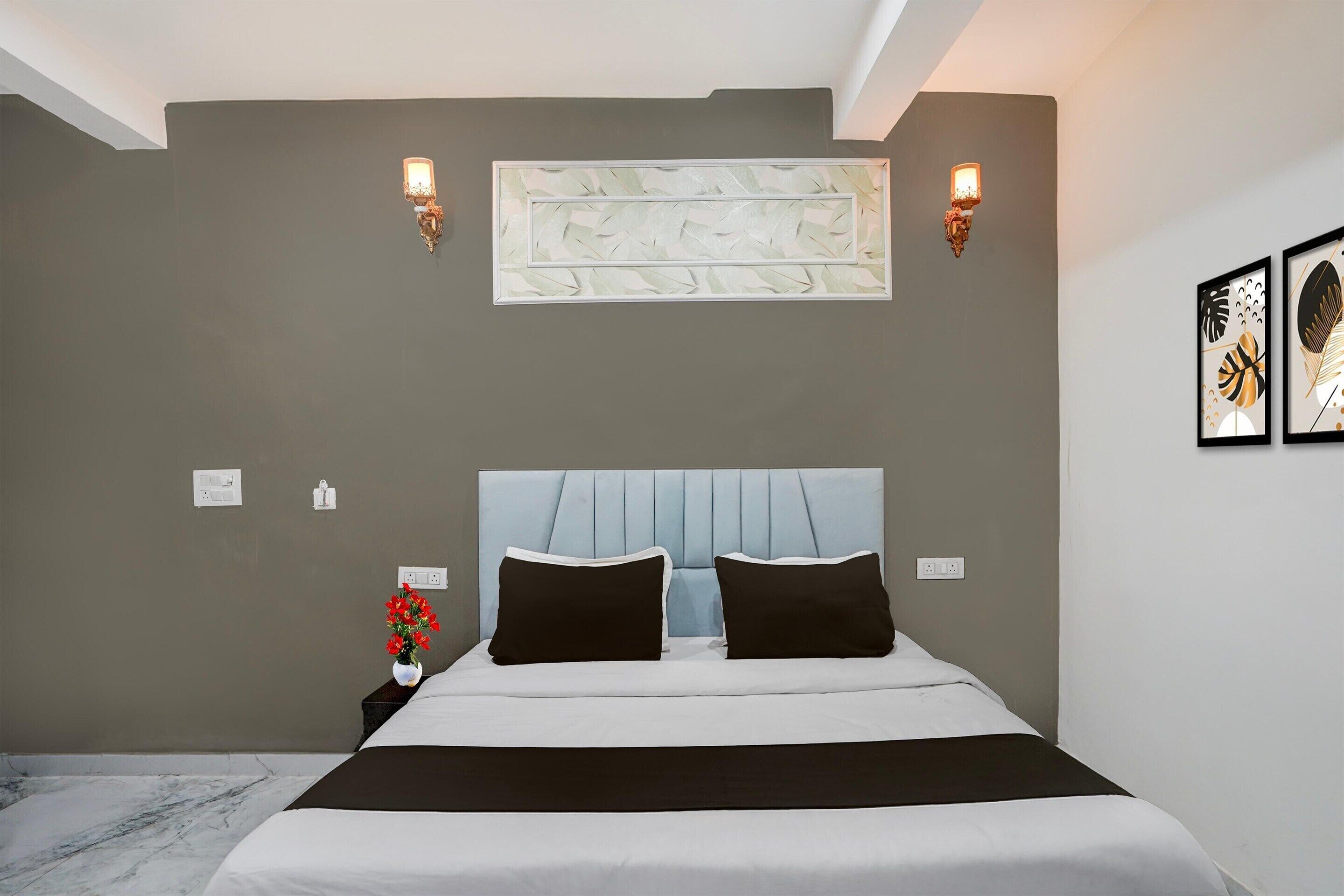 A bedroom with a bed, wall sconces, a vase with flowers, and framed artwork.