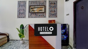 Ein Hotelrezeptionstresen mit einem Schild, das angibt, dass er betriebsbezogen ist. Darüber befinden sich dekorative Wandverkleidungen und links daneben ein Blumentopf.