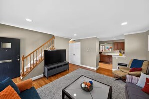 Ein Wohnzimmer mit Fernseher, Sofa, Couchtisch und einer Treppe.