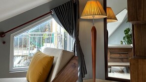 Una habitación con techo inclinado, una ventana con cortinas, una lámpara, un espejo y una planta.