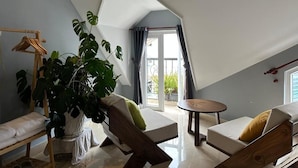 Una habitación estilo loft con techo inclinado, una cama, una silla, una mesa y una planta grande.