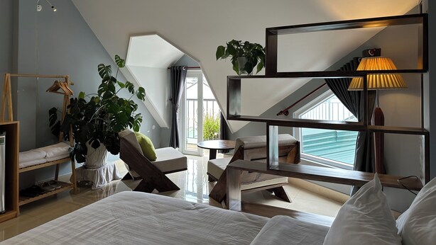 Un dormitorio moderno con techo inclinado, una cama, una silla, una mesita, una lámpara y una planta en maceta.