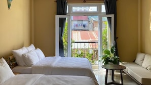 Habitación de hotel con dos camas, un sofá, una mesita y vista a un edificio de tejados rojos a través de un ventanal.
