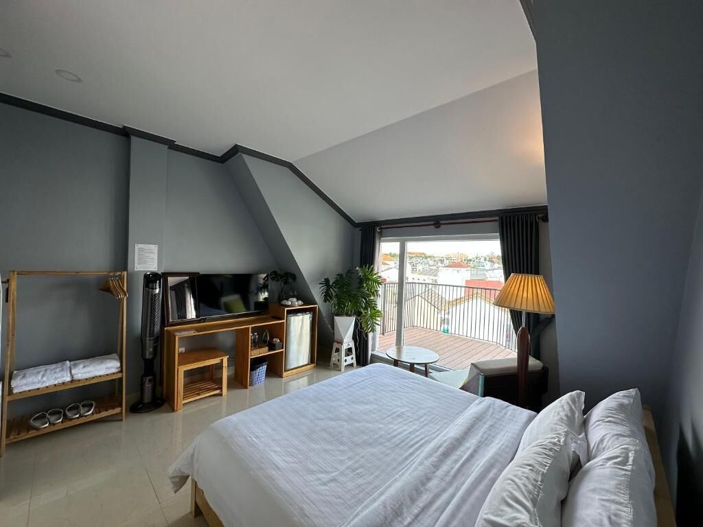 Une chambre d’hôtel moderne dotée d’un grand lit, d’une télévision, d’une petite table, d’un balcon avec vue et d’un plafond agrémenté d’une lucarne.