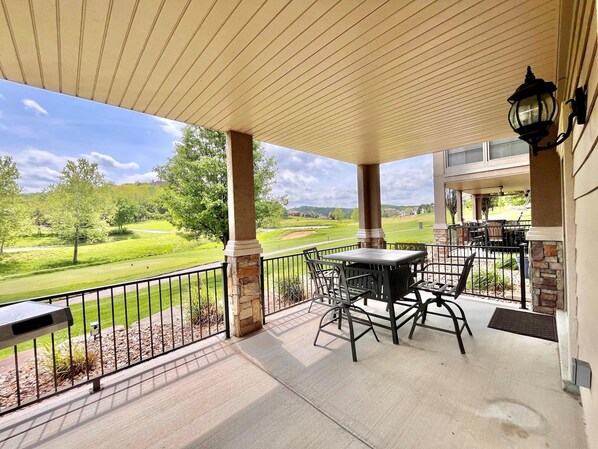 A covered patio with a view of a golf course, outdoor furniture, and a stone pillar.