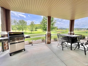 A covered patio with a grill and outdoor seating, overlooking a golf course.