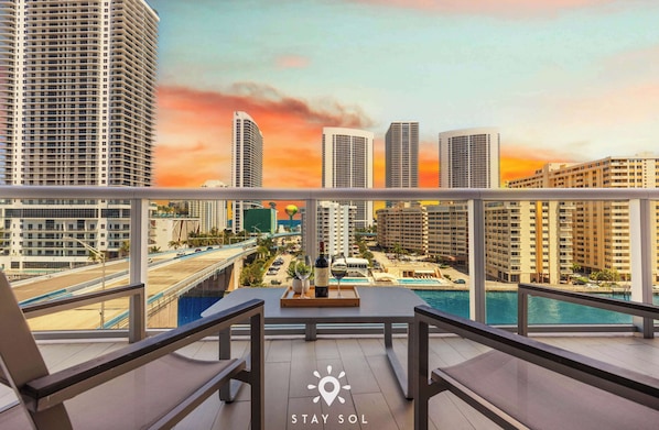 A balcony with a view of a cityscape, a pool, and a table with a bottle and glasses. - New! Haven with Pool and Balcony (Hallandale Beach)