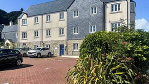 Un hotel de varios pisos con fachada de piedra, numerosas ventanas y un estacionamiento con automóviles.