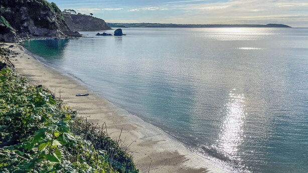 Un paisaje costero con una playa arenosa, mar tranquilo y acantilados rocosos.