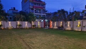 A grassy area with a gated entrance, palm trees, and a building with illuminated signage in the background. - shivaalik (Varanasi)