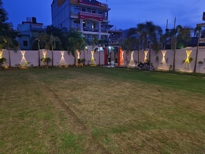 A grassy area with a gated entrance, palm trees, and a building with illuminated signage in the background. - shivaalik (Varanasi)
