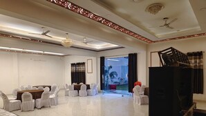 A spacious room with a high ceiling, ceiling fans, a large window with a view, and a stage area with chairs and a table. - shivaalik (Varanasi)
