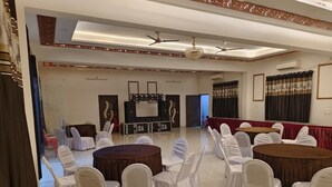 A spacious hall with round tables and chairs, ceiling fans, and a stage area. - shivaalik (Varanasi)