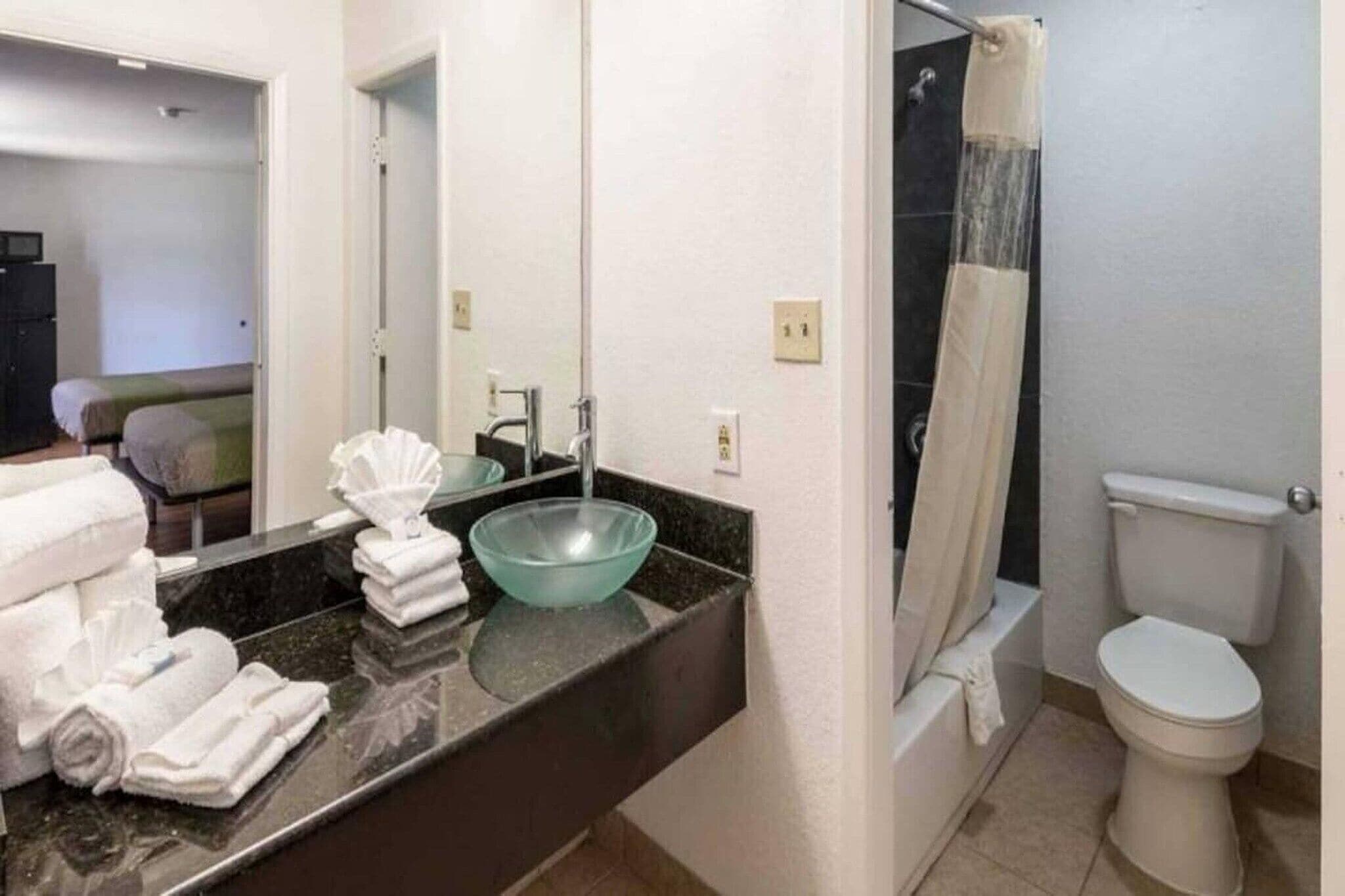A bathroom with a sink, mirror, towel rack, toilet, and shower curtain.