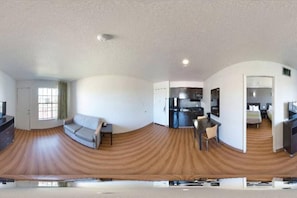 A panoramic view of a hotel room with a wooden floor, a sofa, a dining table, a kitchen area, and a separate bedroom. - 1 King Bed|Suite,Smk,Sofa-Bed (Dallas)
