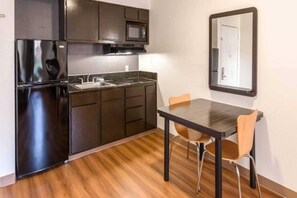 Cocina compacta con refrigerador, microondas, lavaplatos y una mesa de comedor con sillas.